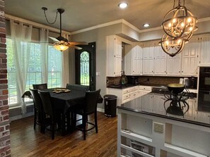 A kitchen with white cabinets, a black island, and a chandelier. - Spacious 4 BR Retreat w/Fitness Center & Golf Simulator (Dallas)