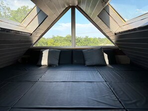 A room with a sloped ceiling, a window with a view of greenery, and a bed with pillows. - Spacious 4 BR Retreat w/Fitness Center & Golf Simulator (Dallas)