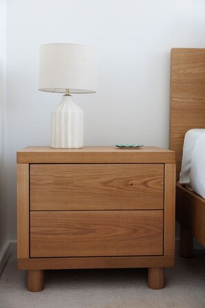 Ein Nachttisch aus Holz mit Lampe und Schublade neben einem Bett mit einem Holz-Kopfende.