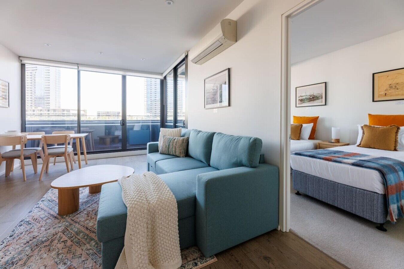 Une chambre d’hôtel moderne dotée d’un canapé, d’un lit, d’un coin repas avec des chaises et une table, ainsi que de grandes fenêtres offrant une vue sur la ville.