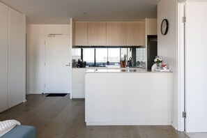 Eine moderne Küche mit Kochinsel, weißen Schränken und Blick auf die Stadt durch große Fenster.