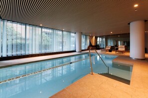 An indoor swimming pool with clear glass walls, a tiled floor, and a ceiling with a wooden slat design. - Marvel & Waterfront Escape - Docklands (Docklands)