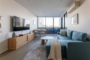 Ein modernes Wohnzimmer mit Flachbildfernseher, einer Couch, einem Couchtisch und einem Essbereich mit Stühlen und Tisch.