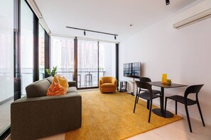 A modern living room with a sofa, armchair, and dining table. - Indi | Chic Inner-City Retreat with Parking (Collingwood)