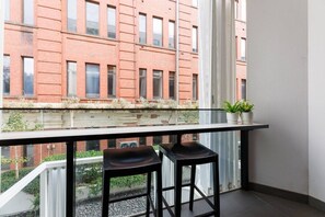 Uma varanda com dois bancos altos pretos, grades de vidro e plantas em vasos.