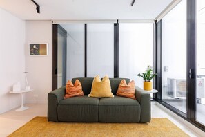 A modern living room with a grey sofa, a small side table, and a potted plant. - Indi | Chic Inner-City Retreat with Parking (Collingwood)