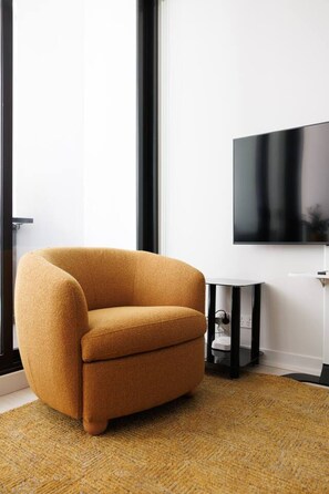 Uma sala de estar moderna com uma poltrona cor mostarda, uma televisão de tela plana na parede e uma pequena mesa lateral preta.