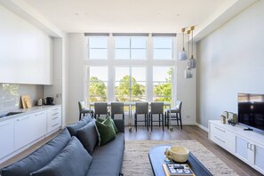 Een moderne keuken met witte kasten, een eethoek met een tafel en stoelen, en een groot raam met uitzicht op bomen.
