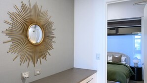 A bedroom with a bed, bedside table, and a wall-mounted mirror with a sunburst design. - Herald Living - Iconic City Heritage Building (Melbourne)