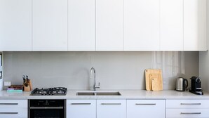 A modern kitchen with white cabinets, a stainless steel sink, a gas stove, and a coffee maker. - Herald Living - Iconic City Heritage Building (Melbourne)