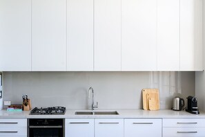 A modern kitchen with white cabinets, a stainless steel sink, a gas stove, and a coffee maker. - Herald Living - Iconic City Heritage Building (Melbourne)