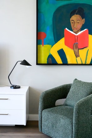 A room with a white nightstand, a black desk lamp, a green armchair, and a colorful abstract painting on the wall. - Herald Living - Iconic City Heritage Building (Melbourne)