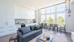 A modern kitchen with white cabinets, a grey sofa, and a dining area with chairs and a table. - Herald Living - Iconic City Heritage Building (Melbourne)