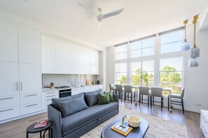 A modern kitchen with white cabinets, a grey sofa, and a dining area with chairs and a table. - Herald Living - Iconic City Heritage Building (Melbourne)