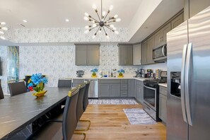 Eine moderne Küche mit grauen Schränken, einem Edelstahlkühlschrank und einem Essbereich mit Holztisch und -stühlen.