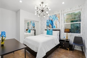 A modern bedroom with a large bed, a desk, a chair, a nightstand, and a large window with a view.