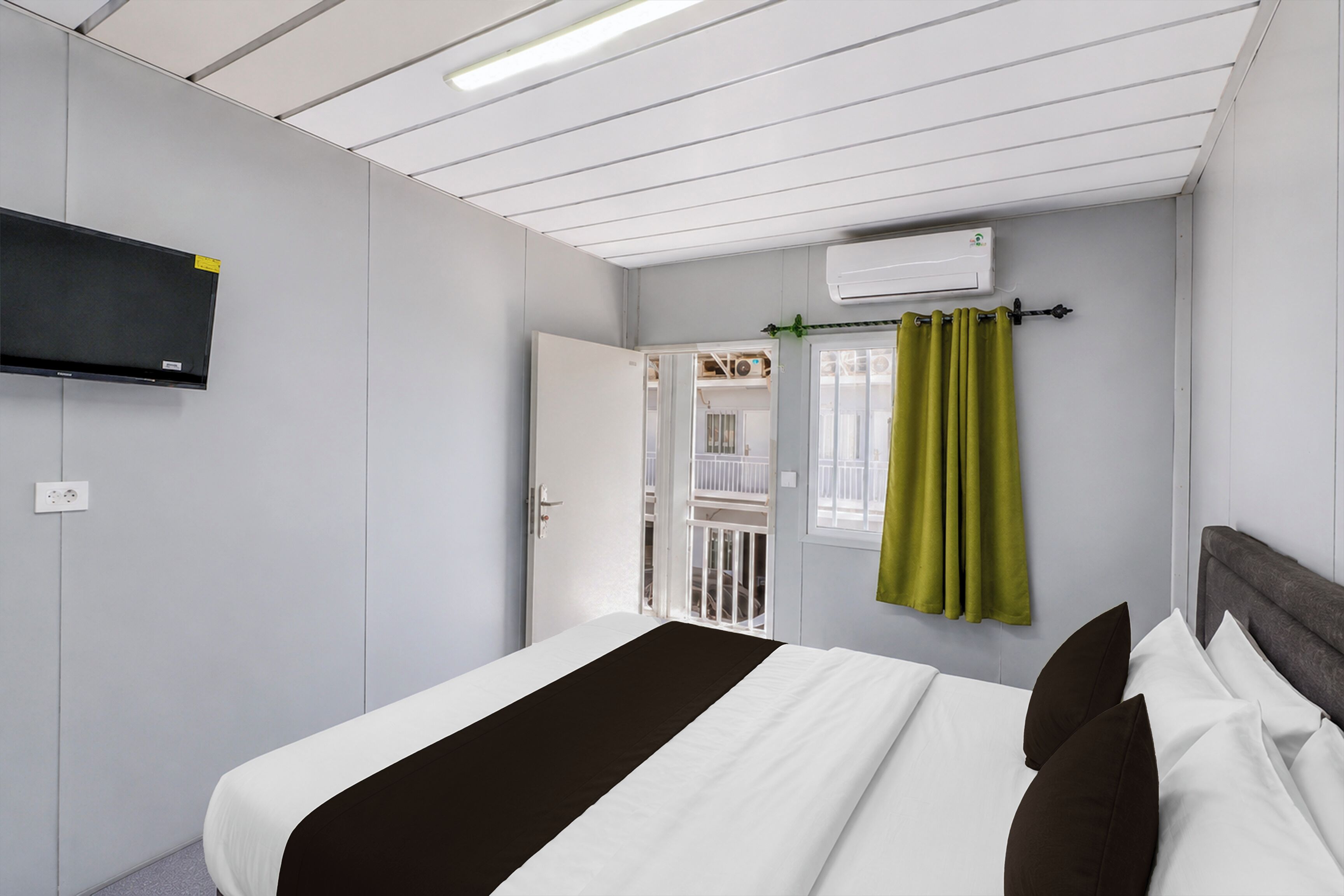 Una habitación de hotel con cama, televisión de pantalla plana montada en la pared, aire acondicionado y ventana con cortinas.