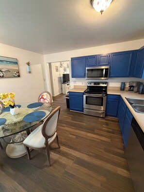 A modern kitchen with blue cabinets, stainless steel appliances, a dining table with blue placemats, and a wooden floor. - Awesome 3-bedroom house in charming downtown Wilmington. Minutes from River Walk (Wilmington)