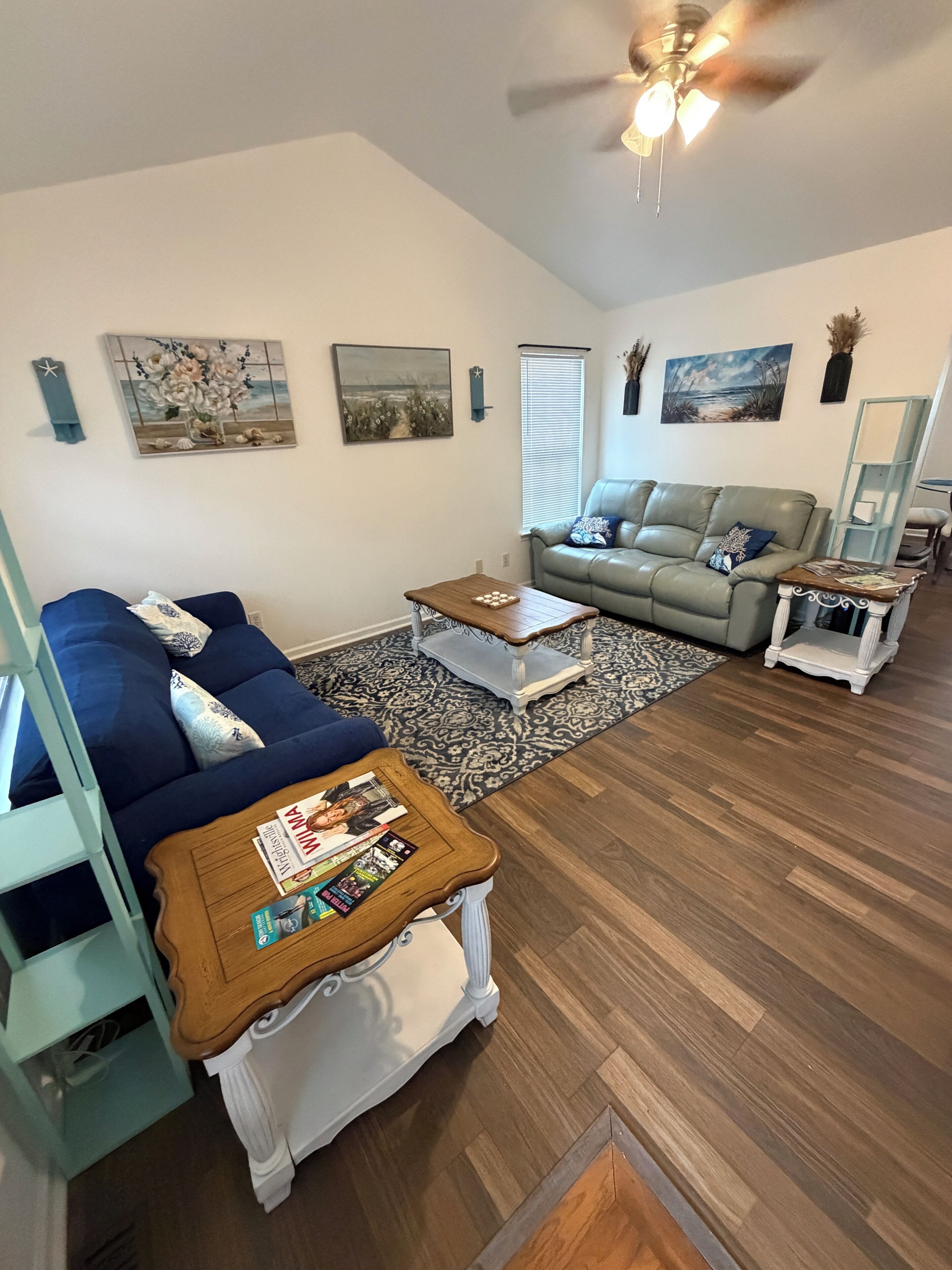 Un soggiorno con un divano blu, un tavolino in legno, un divano grigio e una ventola a soffitto.