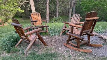 Deux fauteuils Adirondack sont placés dans un espace extérieur verdoyant, avec des arbres en arrière-plan.