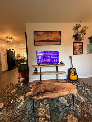 A living room with a flat-screen TV, a guitar, a wooden coffee table, and a patterned rug. - Cozy & eclectic 1BR guest house w/ private entrance & full kitchen. Pet friendly (Lexington)