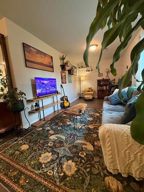 A living room with a television, a guitar, a sofa, and a large plant. - Cozy & eclectic 1BR guest house w/ private entrance & full kitchen. Pet friendly (Lexington)