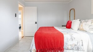 Ein Schlafzimmer mit einem Bett, einer roten Tagesdecke, einer weißen Tür und einem Deckenventilator.