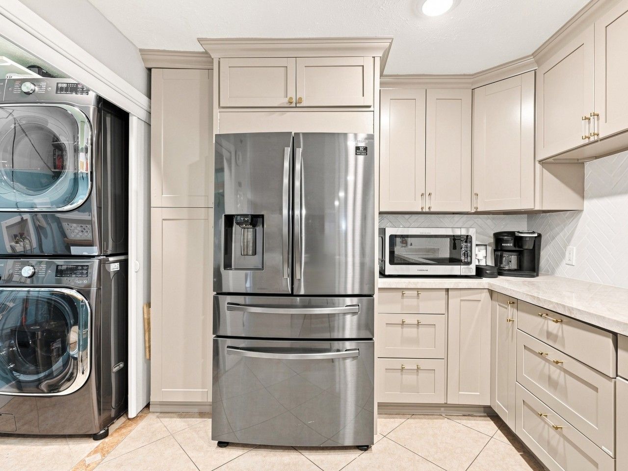 A kitchen with a stainless steel refrigerator, a microwave, a coffee maker, and a washing machine.