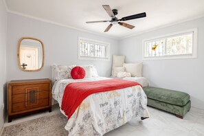A bedroom with a bed, a dresser, a bench, a ceiling fan, and two windows with decorative elements. - The Phoenix Haven Resort Village | Pool & Gym | (Phoenix)