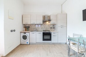 A compact kitchen with a washing machine, oven, and a dining area with a bench. - Casa Roberta - Goelba (Portoferraio)