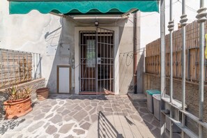 A courtyard with a tiled floor, a metal gate, potted plants, and a green awning. - Casa Roberta - Goelba (Portoferraio)