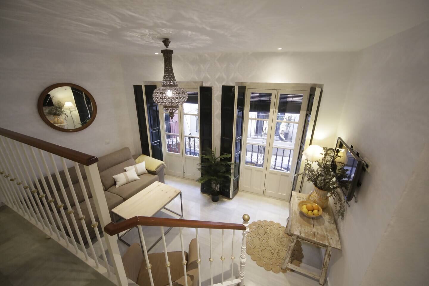 Una sala de estar con sofá, mesa de centro, candelabro, espejo y escalera.