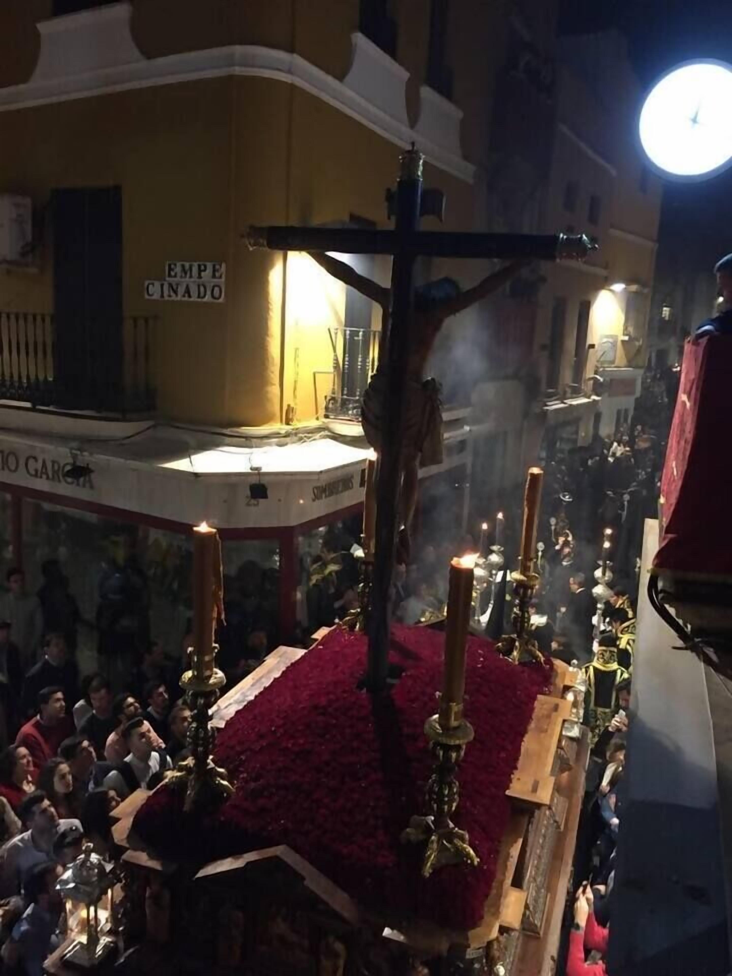 A religious procession with a large cross, candles, and a crowd of people.