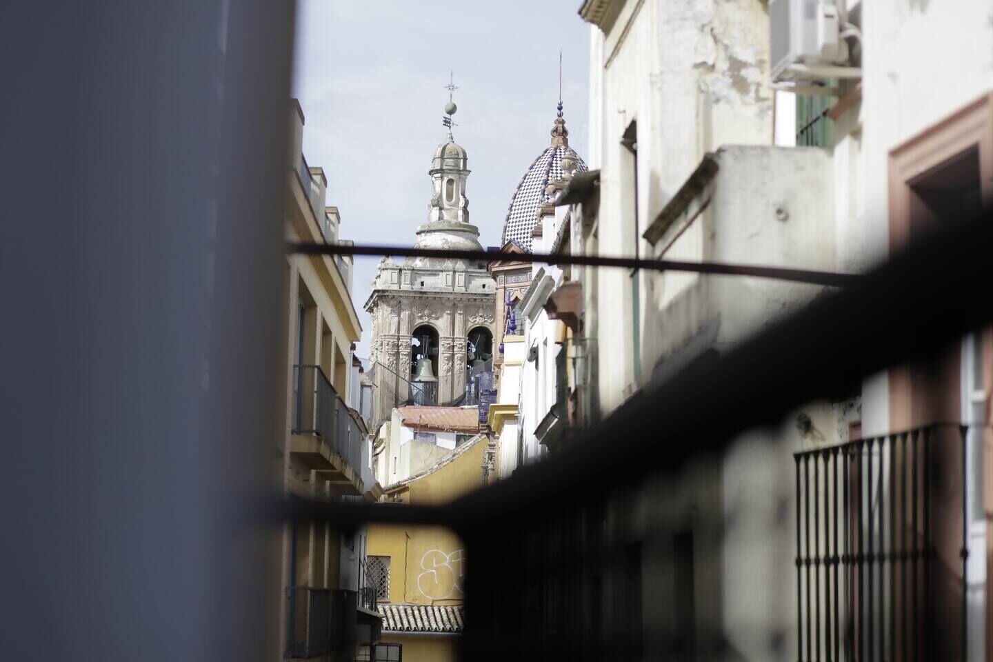 Una calle estrecha flanqueada por edificios, una torre de campanas y un balcón con barandilla.