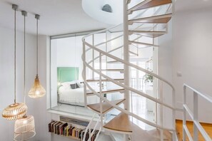 A spiral staircase with a white railing, a bed with a green headboard, and hanging light fixtures. - Impresionante duplex con terraza propia Sevilla (Sevilla)