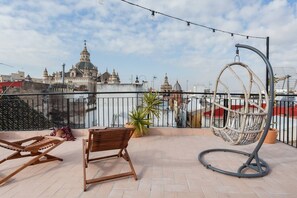 Terraza en la azotea con una silla colgante, un banco de madera y vistas a edificios históricos.
