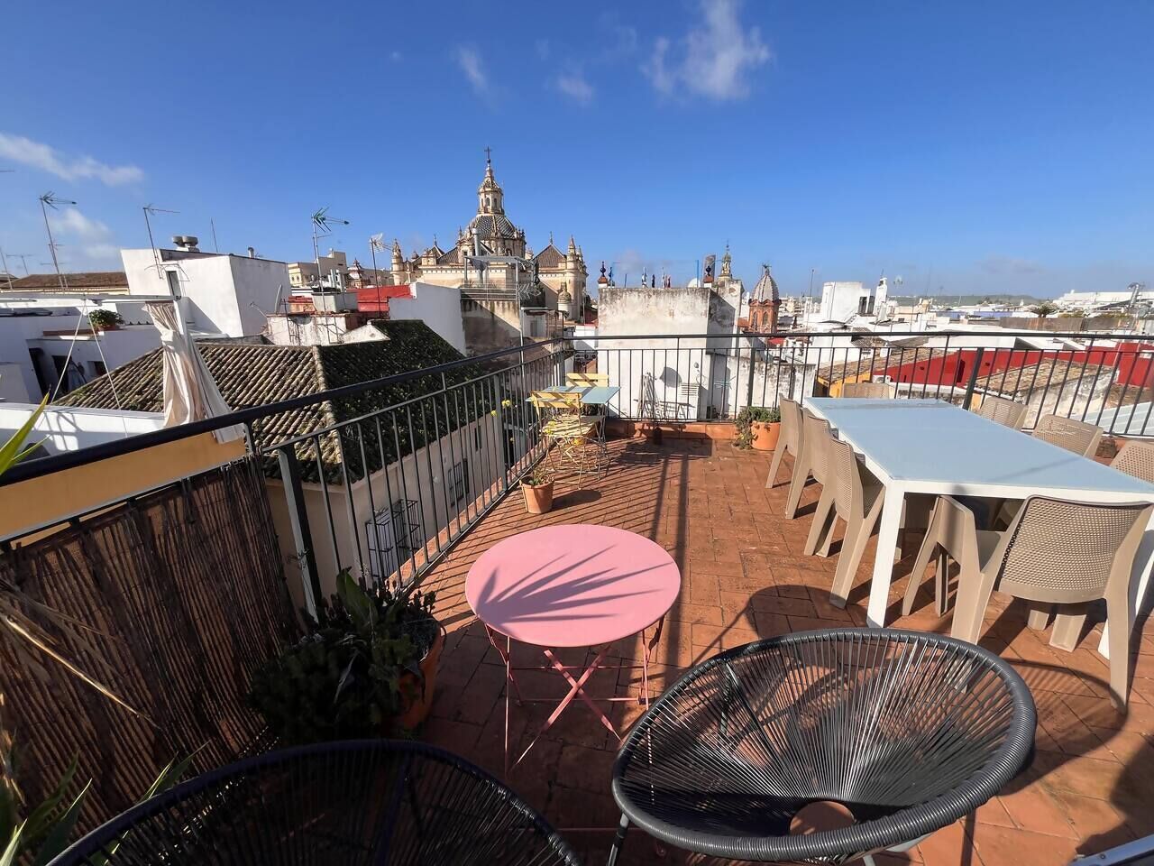 Una terraza en la azotea con una mesa y sillas, vistas a una iglesia y un paisaje urbano al fondo.