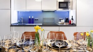 Een moderne keuken met een ingebouwde magnetron, een verlicht eiland in blauw en een eethoek gedekt voor een maaltijd, compleet met wijnglazen en borden.