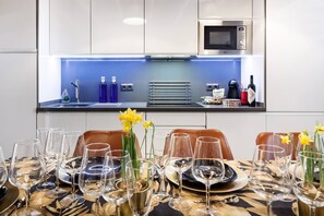 A modern kitchen with a built-in microwave, a blue-lit island, and a dining area set for a meal with wine glasses and plates. - Impresionante duplex con terraza propia Sevilla (Sevilla)