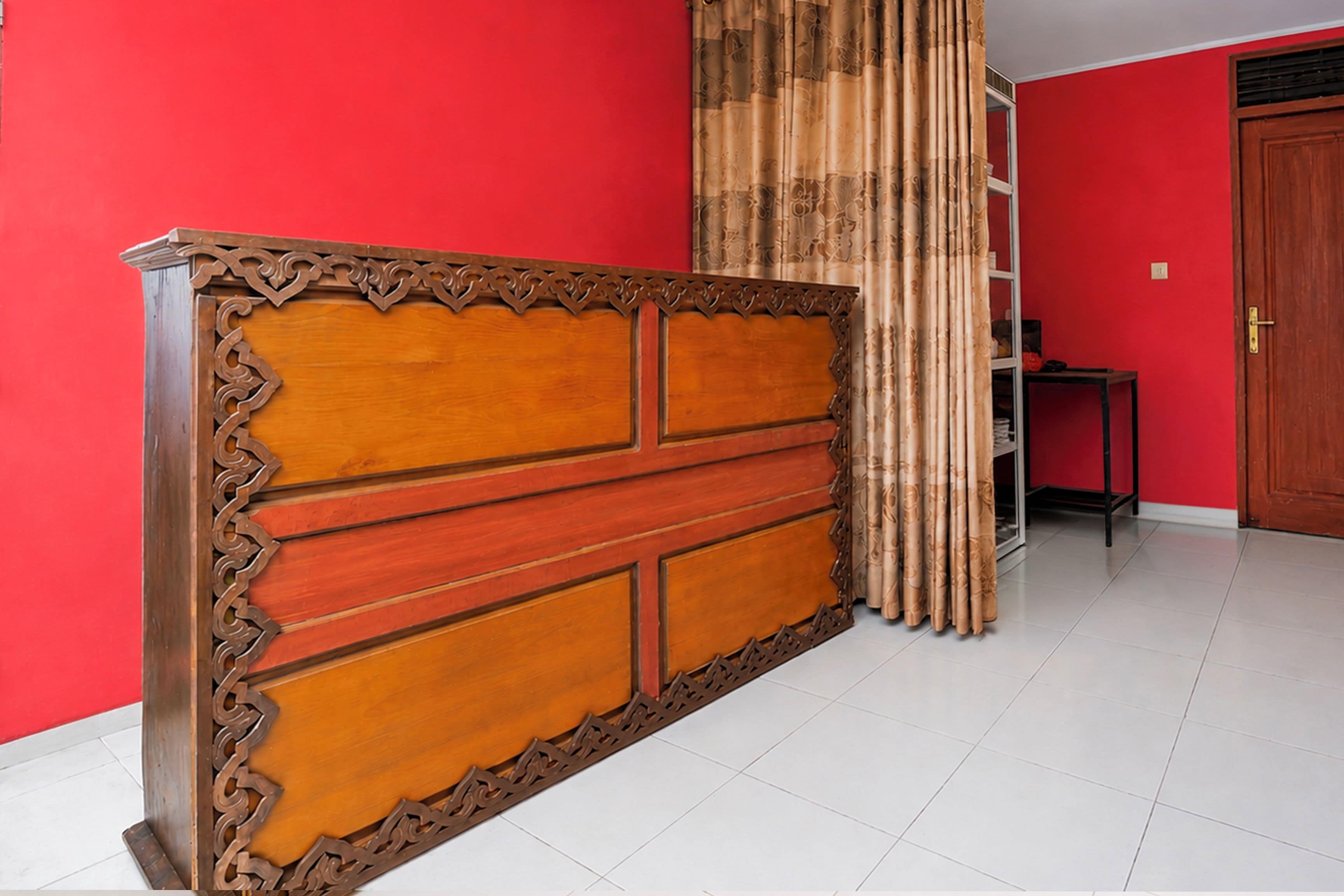 A room with a red wall, a wooden cabinet with intricate carvings, and a bamboo curtain.
