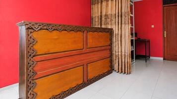 A room with a red wall, a wooden cabinet with intricate carvings, and a bamboo curtain.