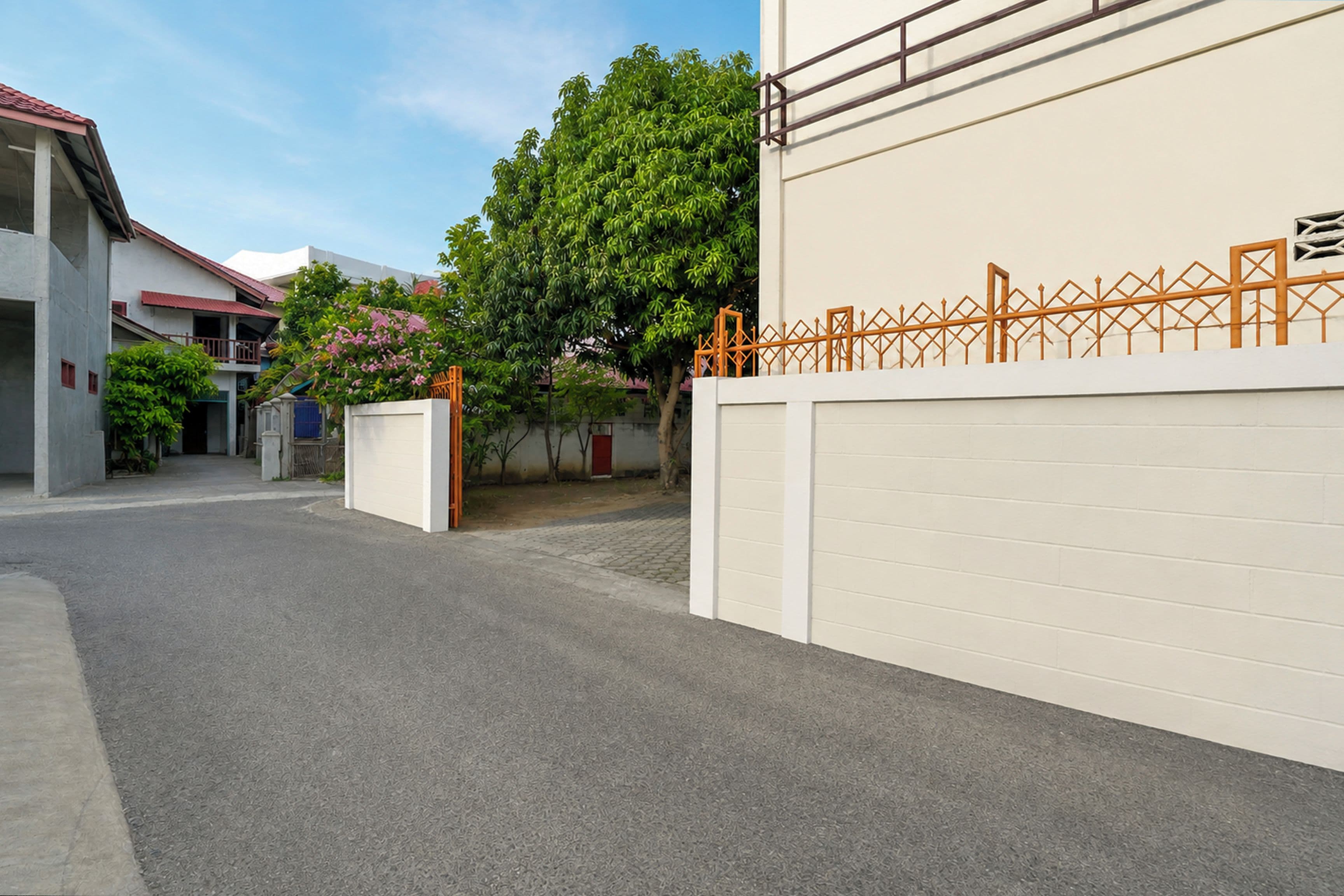 Una calle residencial con una puerta de garaje blanca, una cerca metálica y un árbol con flores rosadas.