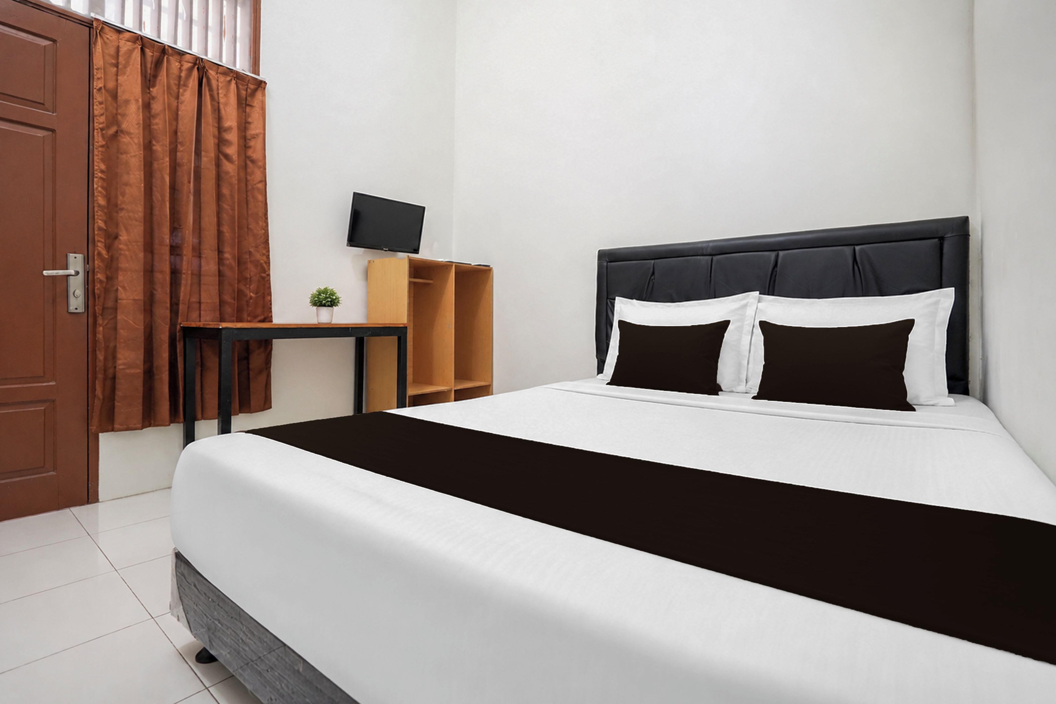 Una habitación de hotel con una cama, un escritorio, un televisor y una ventana con cortinas.