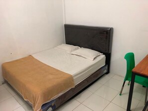 A single bed with a headboard, a green chair, and a wooden table in a room with white walls and tiled flooring.