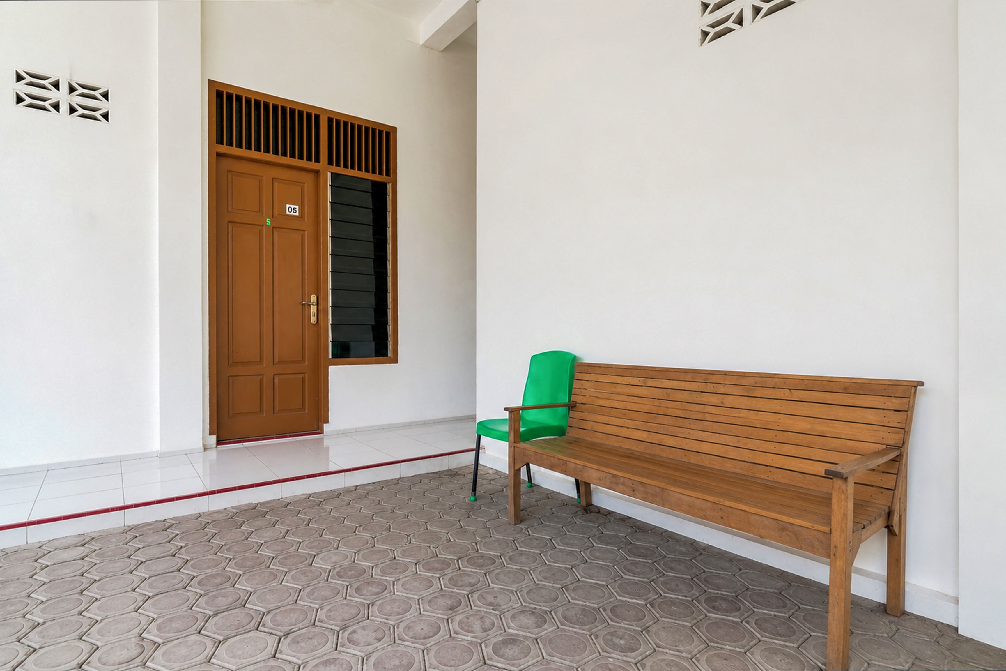 Un pasillo con un banco de madera, una silla verde y una puerta con ventanal.