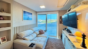 Ein modernes Wohnzimmer mit einer Couch, einem Flachbildfernseher, einer Lampe und Blick durch eine Glastür.