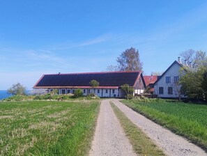 A rural property with a gravel driveway leading to a large house with a red roof and solar panels. - Cosy holiday apartment on Bornholm (Hollændergårde)