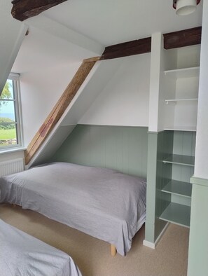 Une chambre avec un plafond en pente, une fenêtre et une bibliothèque intégrée.