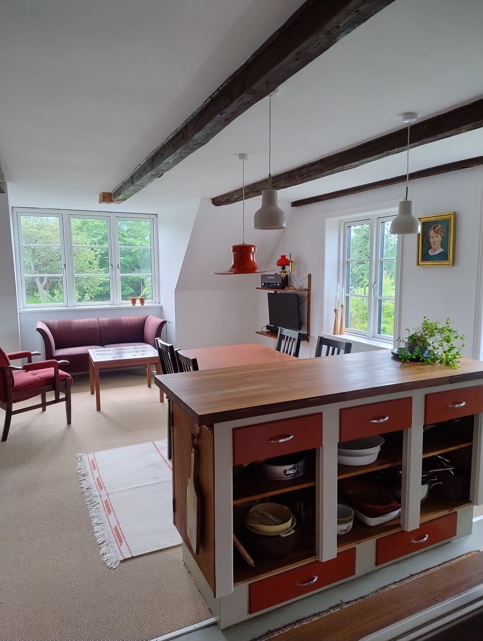 A cozy kitchen with a wooden island, red cabinets, and a red pendant light.