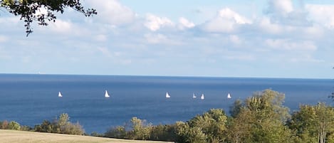 A stone wall with chairs facing a view of the ocean and sailboats.
